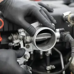 Mechanik w czarnych rękawiczkach sprawdza przepustnicę, szukając oznak nieszczelnej odmy.