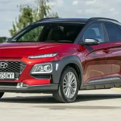 Czerwony, mały SUV dla kobiety, Hyundai Kona, z czarnym dachem, zaparkowany na zewnątrz.