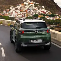 Zielony Citroën C3 Aircross z białym dachem jedzie krętą drogą w górach, z widokiem na kolorowe miasteczko i morze.