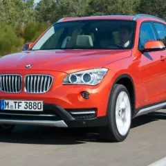 Pomarańczowy BMW X1 E84 jedzie po drodze, za kierownicą siedzi mężczyzna.
