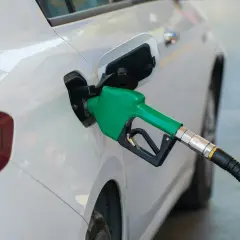 Zielona dysza dystrybutora paliwa wlewa płyn do białego samochodu. Dylemat: benzyna czy diesel?
