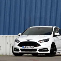 Biały Ford Focus ST z silnikiem 2.0 TDCI, zaparkowany przed niebieską, falistą ścianą.