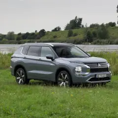 Szary Mitsubishi Outlander PHEV zaparkowany na łące nad jeziorem.