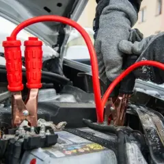 Rękawiczki w szarej zimowej kurtce podłączają kable rozruchowe do akumulatora, pokazując, jak odpalic auto w mroźny dzień.