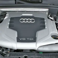 Silnik V6 TDI Audi z widocznym logo i oznaczeniem pojemności. Pod maską widać elementy układu dolotowego i płyny eksploatacyjne.