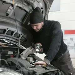 Mechanik z latarką bada silnik Renault, szukając przyczyny błędu DTC P0300.