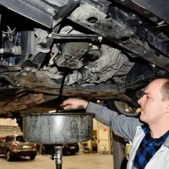 Mechanik wymienia olej w samochodzie, zbierając zużyty płyn do miski.
