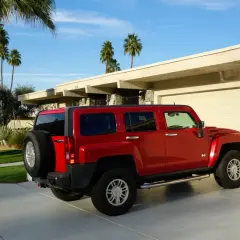 Czerwony Hummer H3 zaparkowany przed domem z palmami w tle.