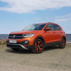 Pomarańczowy Volkswagen T-Cross stoi nad jeziorem, gotowy na letnią przygodę.