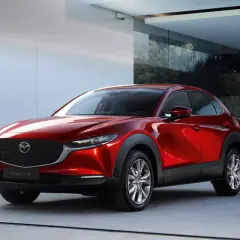 Elegancka, czerwona Mazda CX-30 błyszczy przed nowoczesnym budynkiem z dużymi oknami.