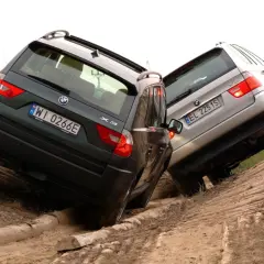 Dwa BMW E83, zielone i srebrne, pokonują trudny teren, wspinając się po piaszczystym zboczu z drewnianymi przeszkodami.