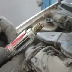 Ręka w rękawicy trzyma świecę zapłonową. Może to być związane z błędem DTC P1604 Toyota.