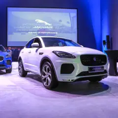 Biały i niebieski Jaguar E-Pace na prezentacji. Na ekranie w tle logo Jaguara i napis "Introducing the new Jaguar E-Pace".