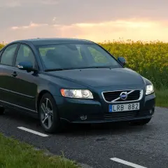 Ciemnozielone Volvo S40 2.0 diesel jedzie wiejską drogą pośród kwitnącego rzepaku o zachodzie słońca.