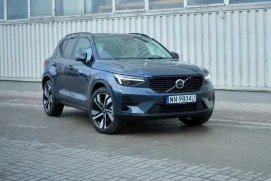 Elegancki, ciemnogranatowy Volvo XC40 2021 z charakterystycznymi światłami LED i felgami, zaparkowany przed budynkiem.