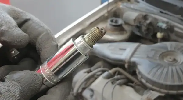 Ręka w rękawicy trzyma świecę zapłonową, być może przyczynę błędu dtc p0301 w Audi. Silnik w tle.
