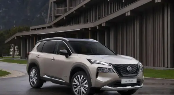 Elegancki, beżowy Nissan X-Trail 2015 zaparkowany przed nowoczesnym budynkiem w górach.