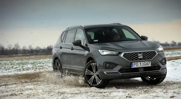 Szary Seat Tarraco SUV przemierza błotniste, zaśnieżone pole, wzbijając chmury brudu.