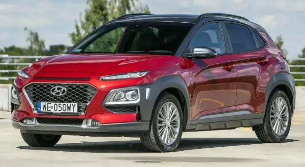 Czerwony, mały SUV dla kobiety, Hyundai Kona, z czarnym dachem, zaparkowany na zewnątrz.