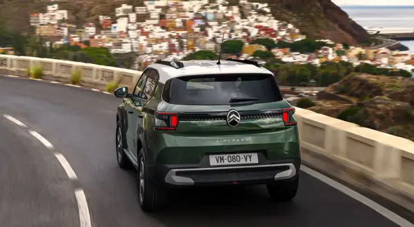 Zielony Citroën C3 Aircross z białym dachem jedzie krętą drogą w górach, z widokiem na kolorowe miasteczko i morze.