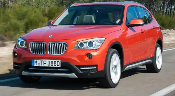 Pomarańczowy BMW X1 E84 jedzie po drodze, za kierownicą siedzi mężczyzna.