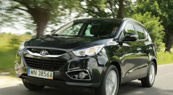 Czarny Hyundai ix35 2.0 benzyna w ruchu, z zielenią drzew w tle.