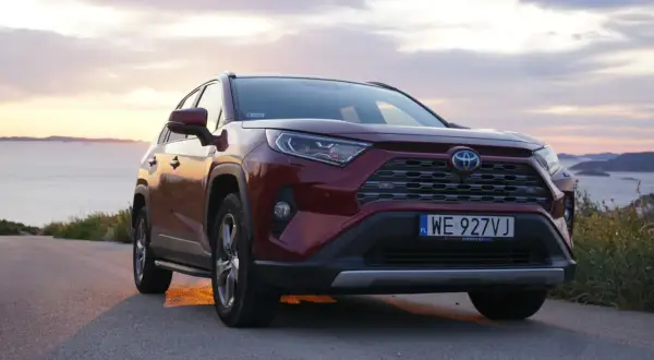 Czerwona Toyota RAV4 2.5 Hybrid na tle zachodzącego słońca nad morzem. Niskie spalanie to jej atut.