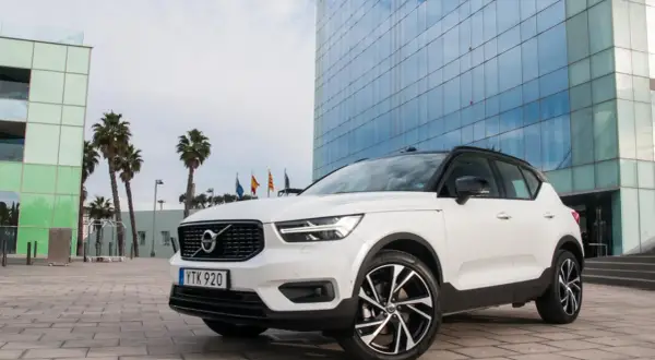 Białe Volvo XC40 z czarnym dachem zaparkowane przed nowoczesnym budynkiem z niebieskimi oknami.