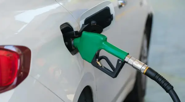 Zielona dysza dystrybutora paliwa wlewa płyn do białego samochodu. Dylemat: benzyna czy diesel?
