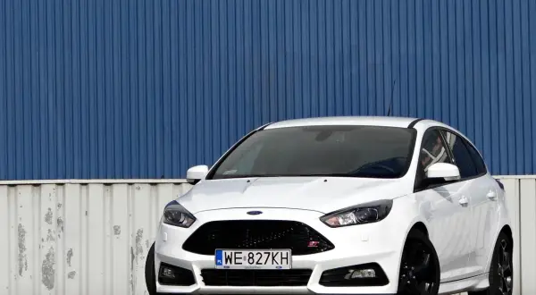 Biały Ford Focus ST z silnikiem 2.0 TDCI, zaparkowany przed niebieską, falistą ścianą.