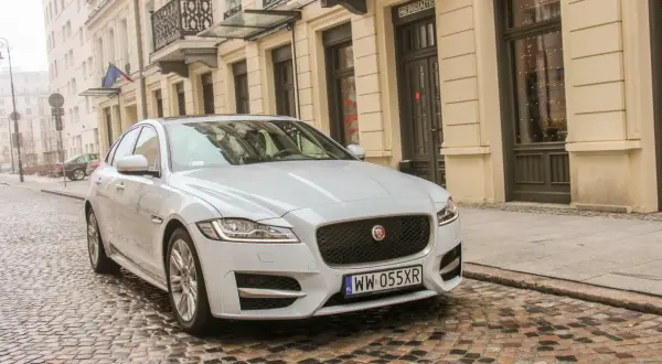 Biały Jaguar XF 3.0 Diesel na brukowanej ulicy przed kamienicą.