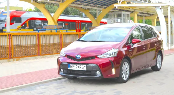 Czerwony Toyota Prius Plus stoi na peronie obok pociągu.