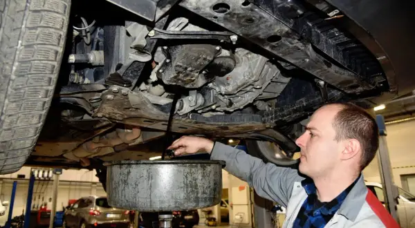 Mechanik wymienia olej w samochodzie, zbierając zużyty płyn do miski.