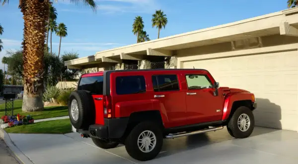 Czerwony Hummer H3 zaparkowany przed domem z palmami w tle.