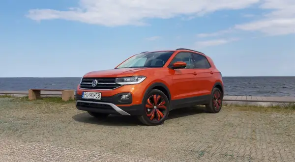 Pomarańczowy Volkswagen T-Cross stoi nad jeziorem, gotowy na letnią przygodę.