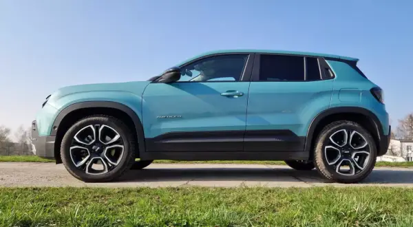Turkusowy suv premium Jeep Avenger z czarnymi akcentami i felgami stoi na tle błękitnego nieba.