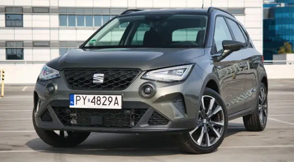 Szary Seat Arona 1.0 TSI zaparkowany przed nowoczesnym budynkiem.