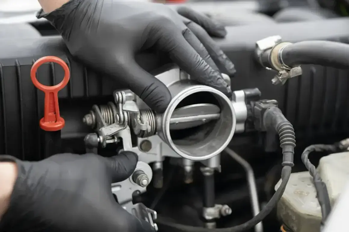 Mechanik w czarnych rękawiczkach sprawdza przepustnicę, szukając oznak nieszczelnej odmy.