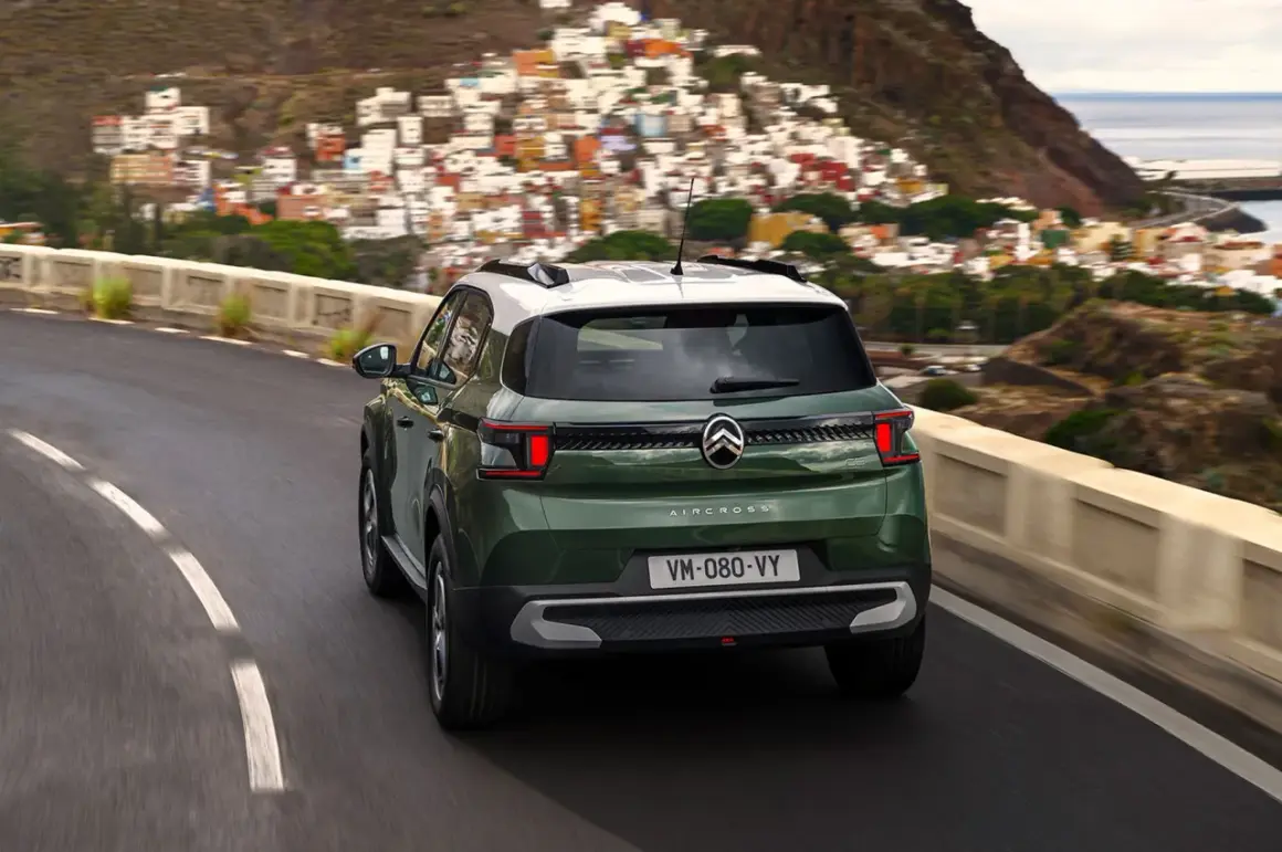 Zielony Citroën C3 Aircross z białym dachem jedzie krętą drogą w górach, z widokiem na kolorowe miasteczko i morze.