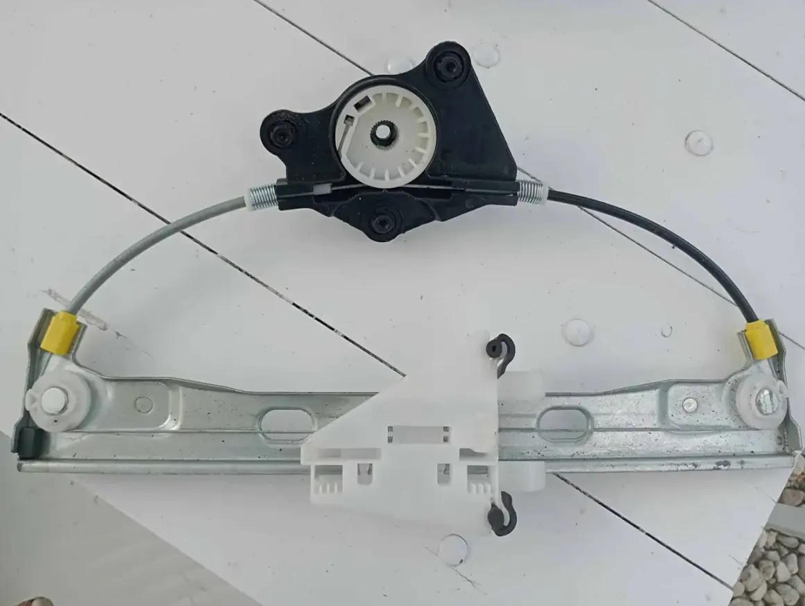 Mechanizm podnoszenia szyby, gotowy do wymiany. Składa się z metalowej szyny, linek i plastikowych elementów.