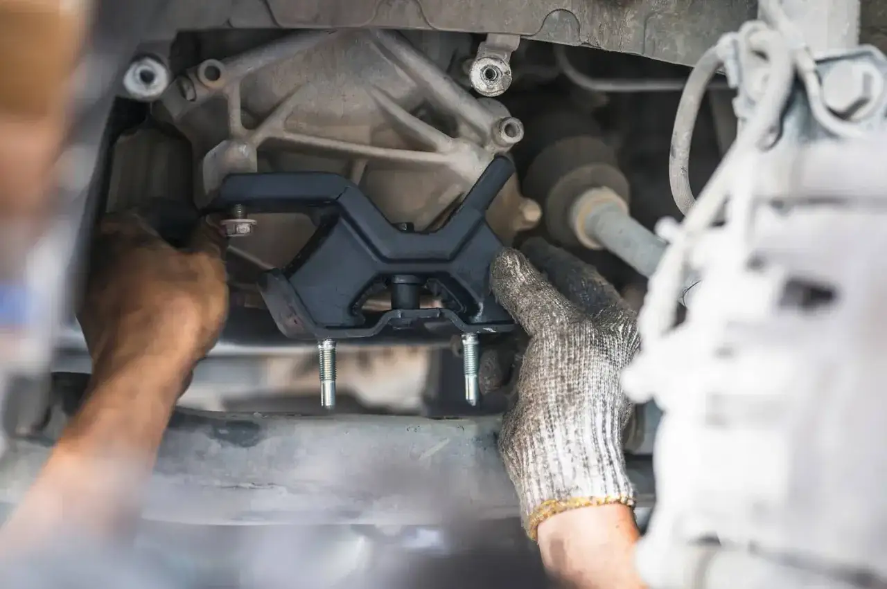 Mechanik wymienia poduszkę silnika, mocując ją do skrzyni biegów.