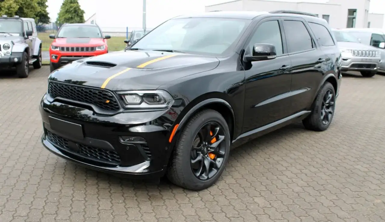 Czarny Dodge Durango 5.7 Hemi z żółtymi pasami na masce, zaparkowany na placu z innymi samochodami.