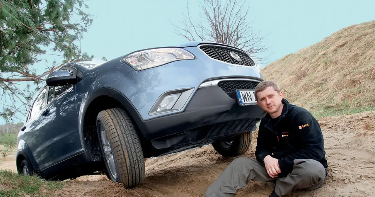 Mężczyzna siedzi obok Ssangyong Korando, który wspina się po piaszczystym zboczu.