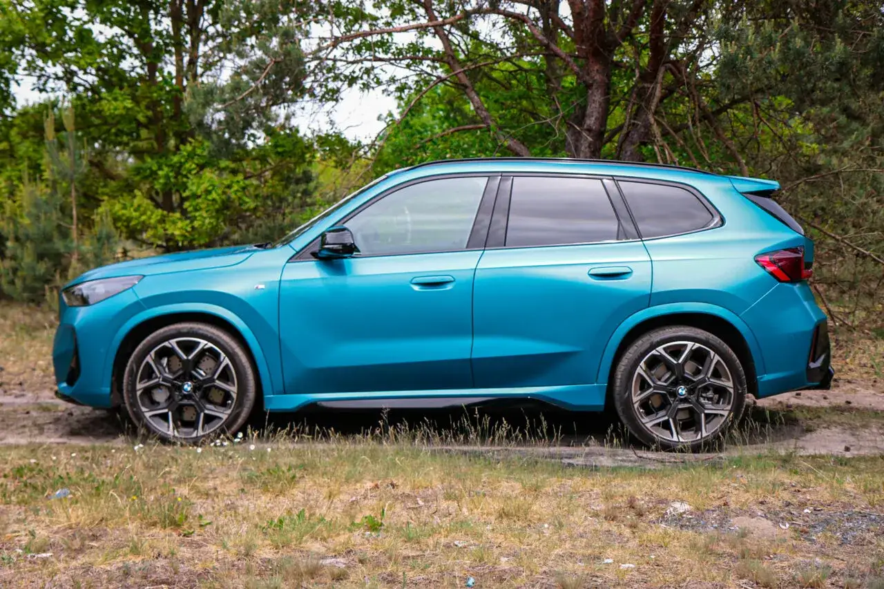 Nowy BMW X1 E84 w turkusowym kolorze, zaparkowany na leśnej polanie, gotowy na przygodę.