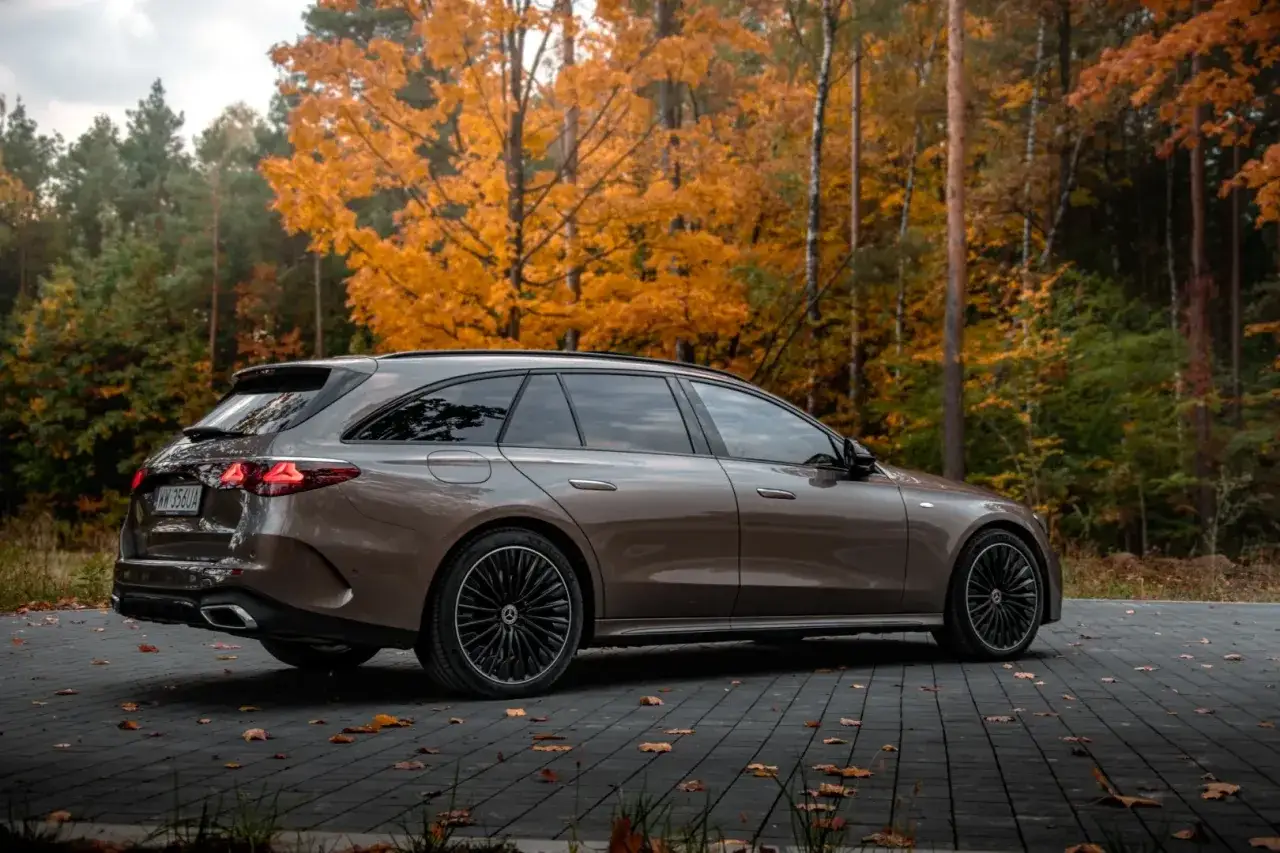 Brązowy Mercedes E300de na tle jesiennego lasu. Elegancki kombi zgrabnie wpasowuje się w krajobraz.