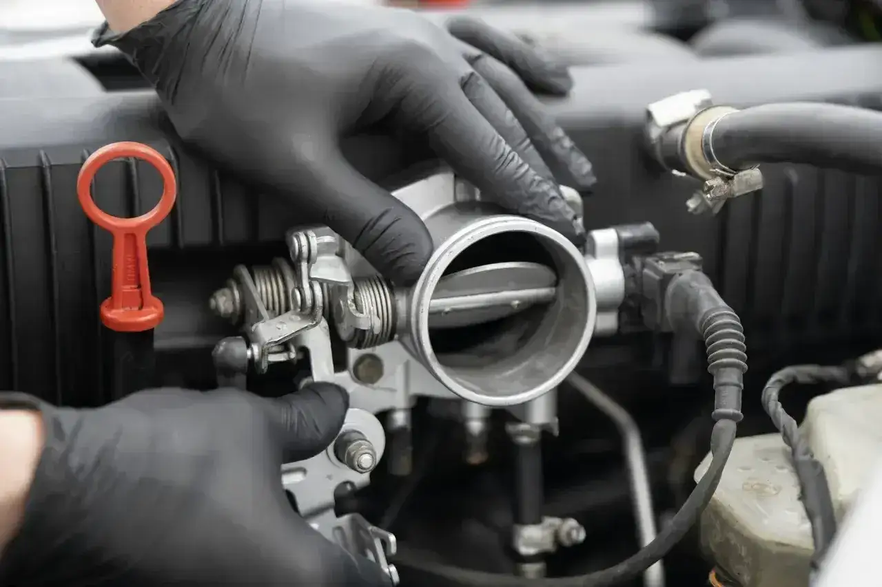 Mechanik w czarnych rękawiczkach sprawdza przepustnicę, która może być przyczyną nieszczelnej odmy i jej objawów.