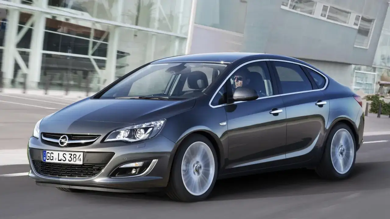 Elegancki, ciemnoszary Opel Astra J 1.7 CDTI w ruchu miejskim. Kierowca w okularach przeciwsłonecznych.