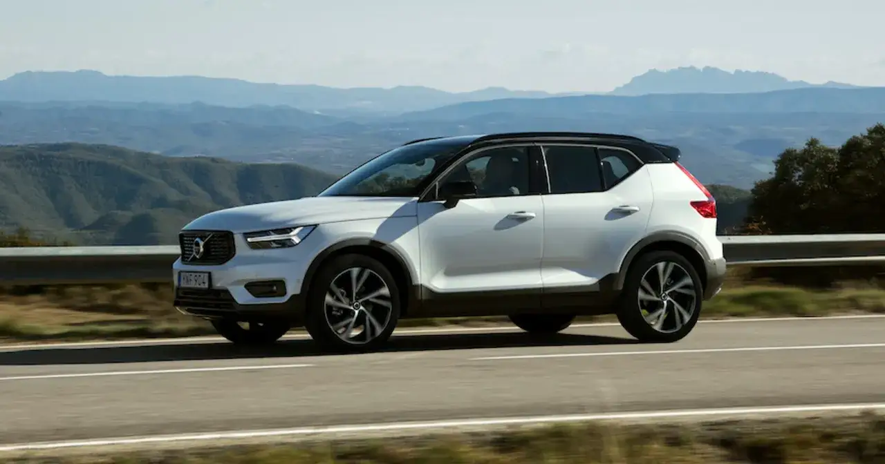 Białe Volvo XC40 z czarnym dachem jedzie po krętej drodze w górach.