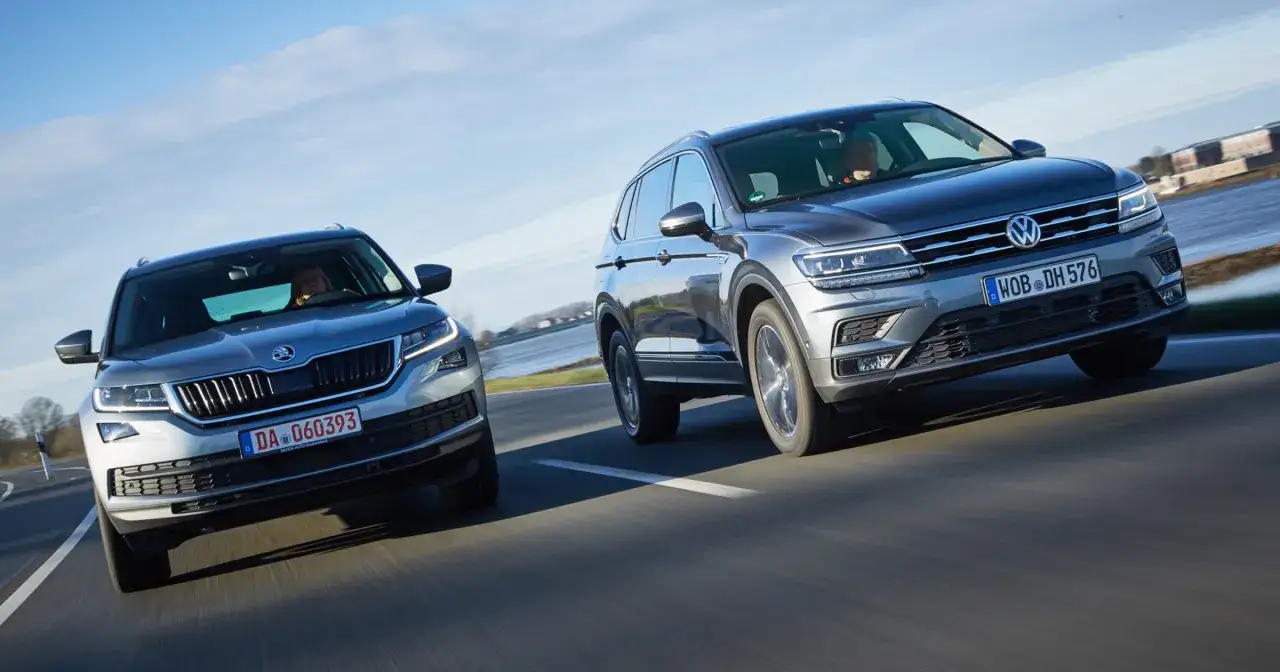 Dwa SUV-y jadące obok siebie: srebrna Skoda Kodiaq i szary Volkswagen Tiguan. Oba modele oferują różne skoda kodiaq silniki.