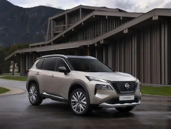Elegancki, beżowy Nissan X-Trail 2015 zaparkowany przed nowoczesnym budynkiem w górach.